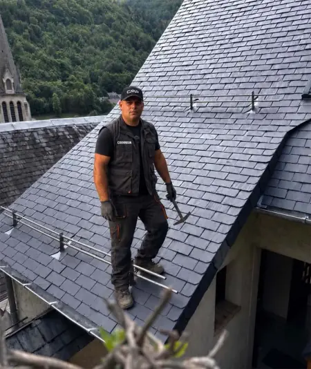 Artisan couvreur sur une toiture en ardoise naturelle dans le Béarn, près de Pau