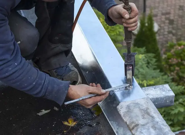 Zingueur soudant à l'étain un chéneau en zinc sur une toiture